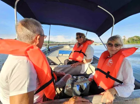Tres viajeros con chalecos naranjas bajo el toldo de un bote en el agua del tour panama monkey island