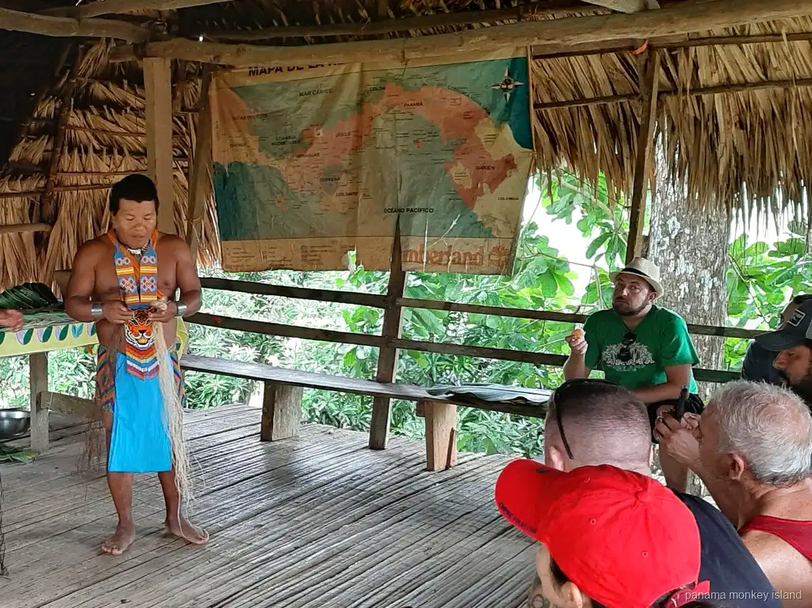 Guía Emberá con vestimenta tradicional hablando a los visitantes bajo un techo de paja en un tour a la isla de los monos Panamá