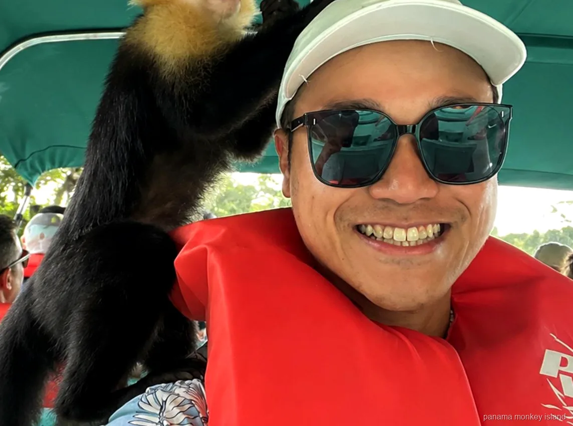 Visitante sonriente con chaleco salvavidas y un mono capuchino en el hombro bajo el toldo en panama monkey island