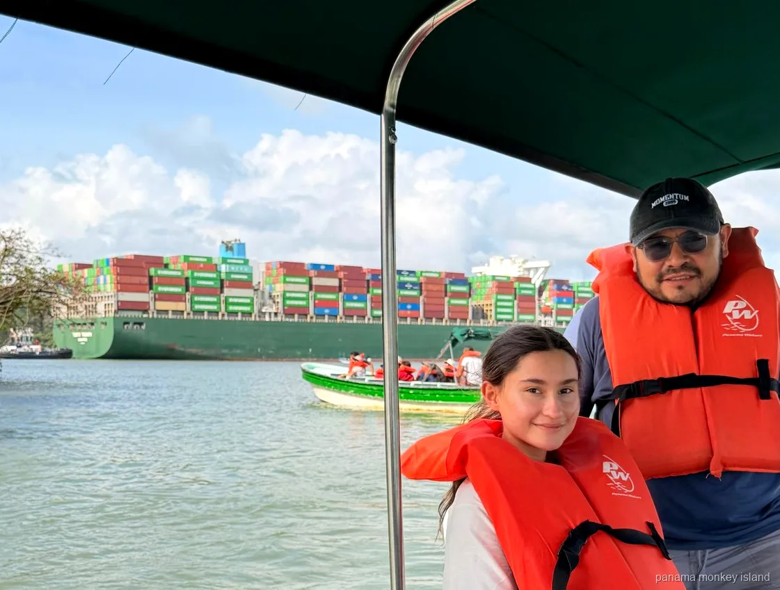 Dos viajeros con chalecos salvavidas ven un gran buque portacontenedores cruzar el Canal en un tour panama monkey island
