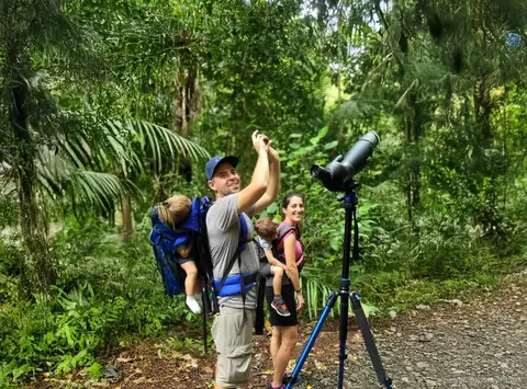 Familia con un telescopio de observación en un sendero del bosque buscando fauna, tour de selva isla de los monos Panamá